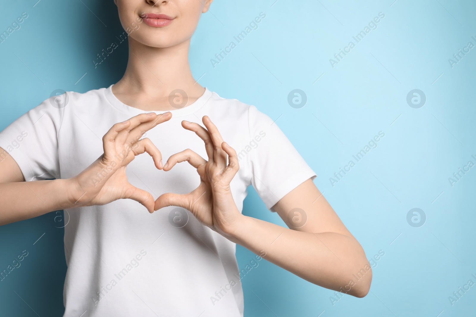 Photo of Woman making heart with hands on light blue background, closeup. Space for text