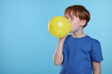 Boy inflating yellow balloon on light blue background, space for text