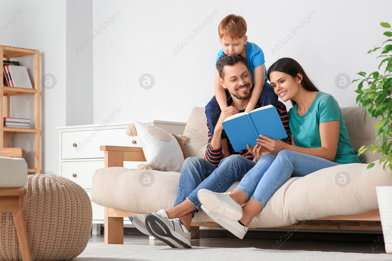 Photo of Happy family reading book together on sofa in living room at home