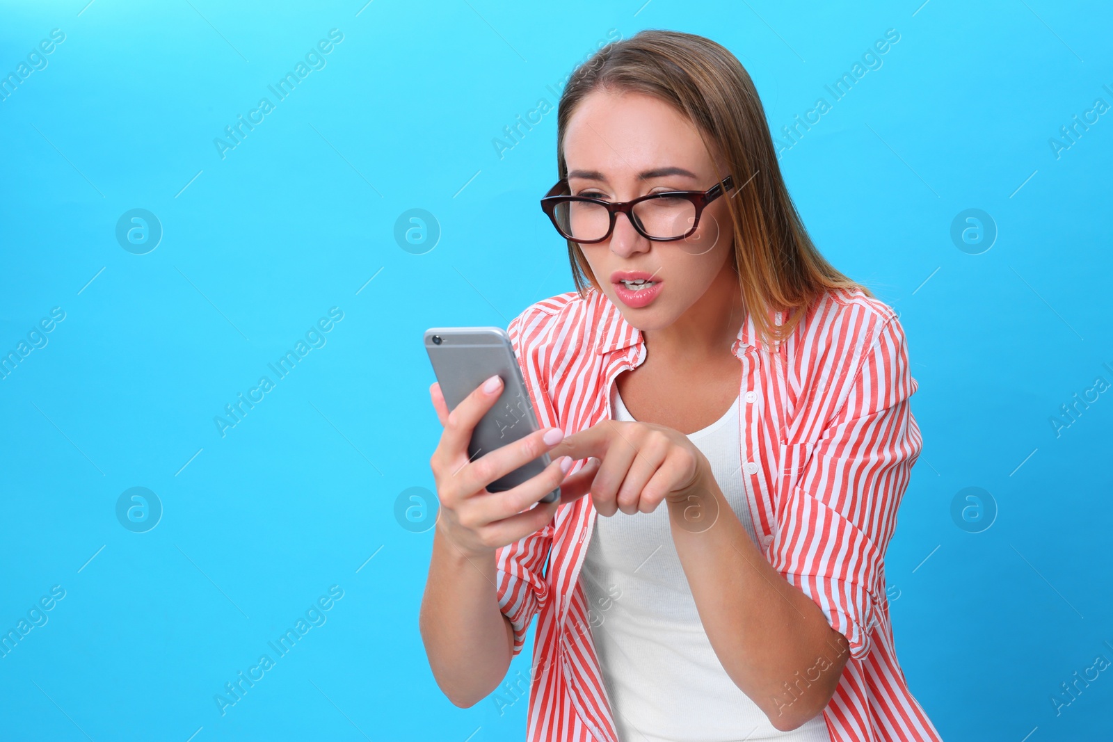 Photo of Young woman with glasses using mobile phone on blue background. Vision problem