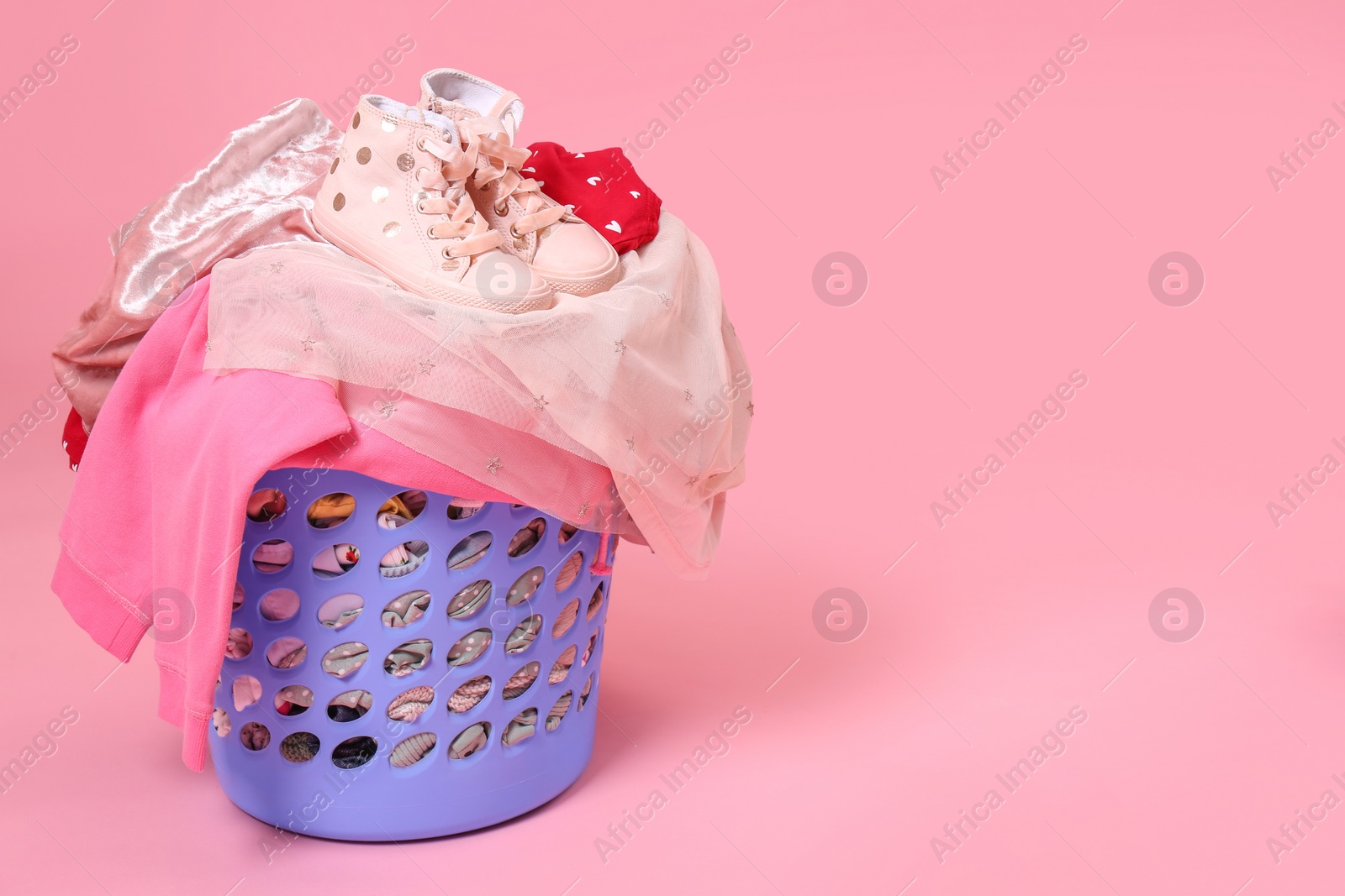 Photo of Laundry basket with baby clothes and shoes on light pink background. Space for text