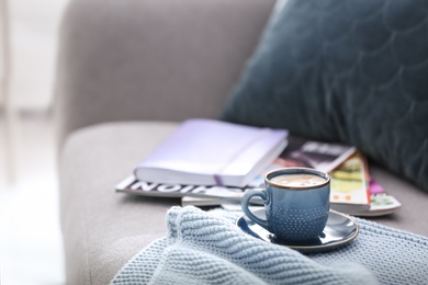 Cup of coffee, plaid and magazines on sofa