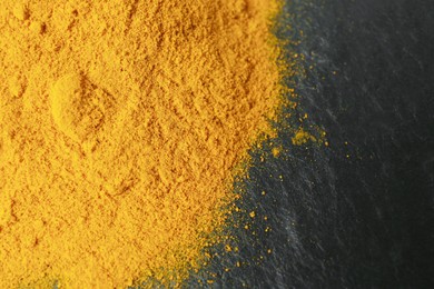 Photo of Turmeric powder on black textured table, closeup