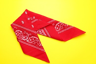 Photo of Folded red bandana with paisley pattern on yellow background, top view