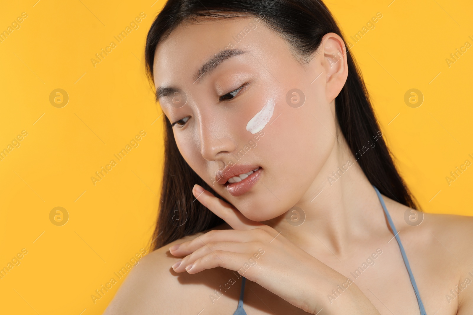 Photo of Beautiful young woman with sun protection cream on her face against orange background, space for text