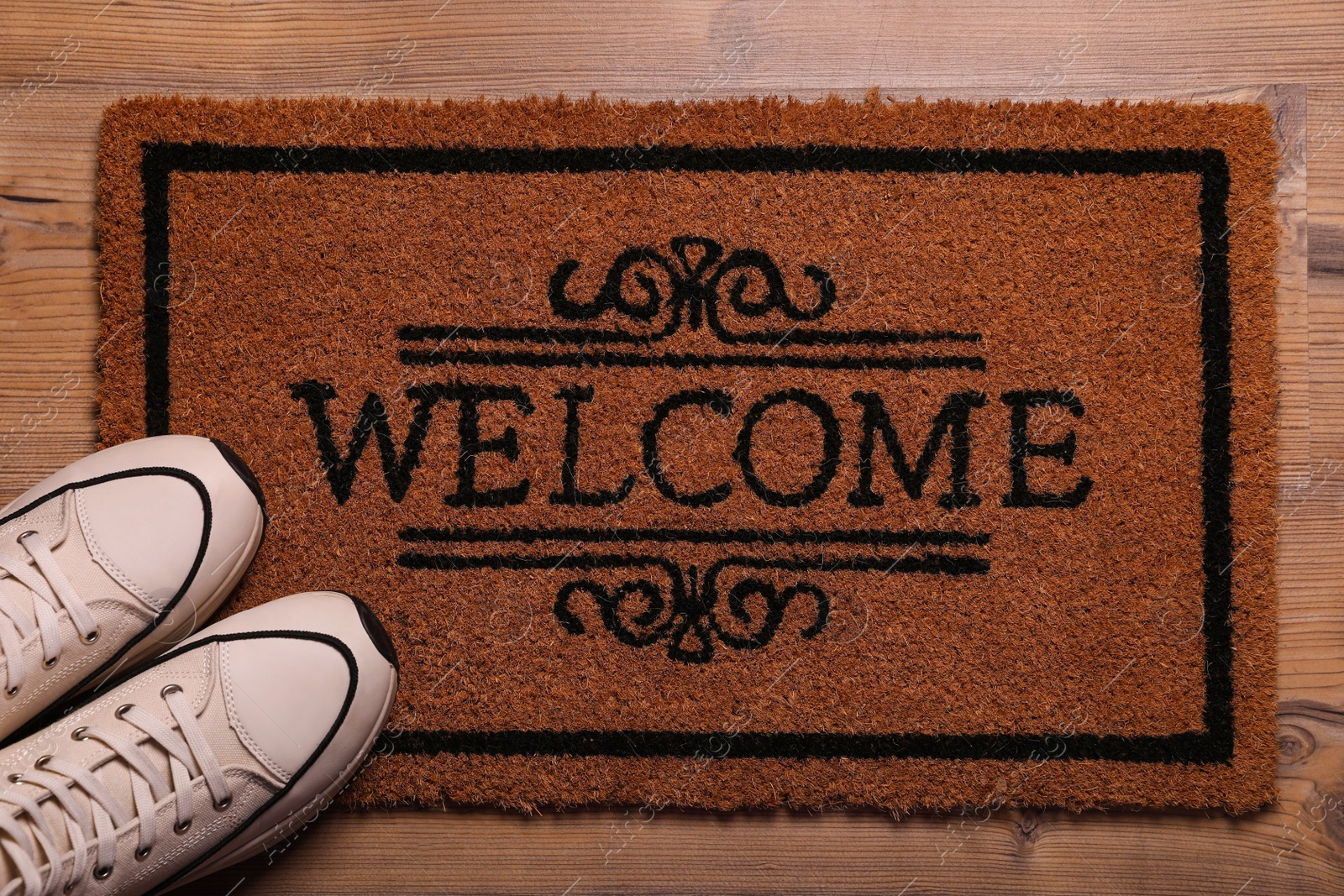 Photo of Door mat with word Welcome and stylish sneakers on wooden floor, flat lay
