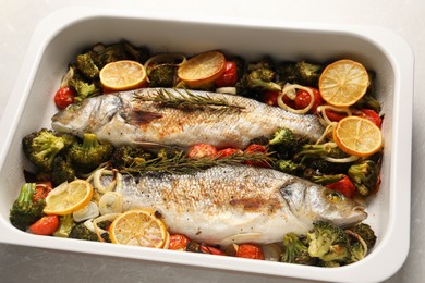 Photo of Delicious fish with vegetables and lemon in baking dish on light marble table