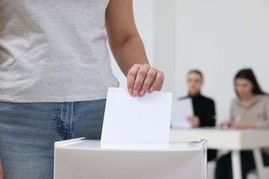 Photo of Woman putting her vote into ballot box on blurred background, closeup