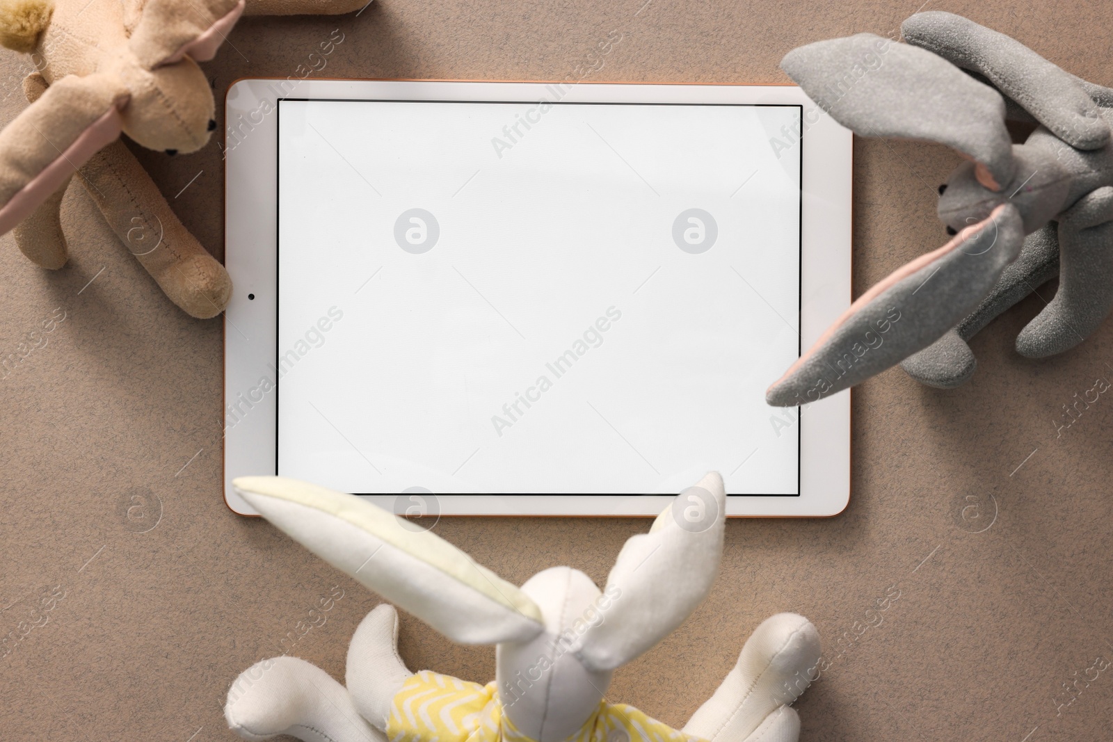 Photo of Modern tablet and kid's toys on light brown background, flat lay. Space for text