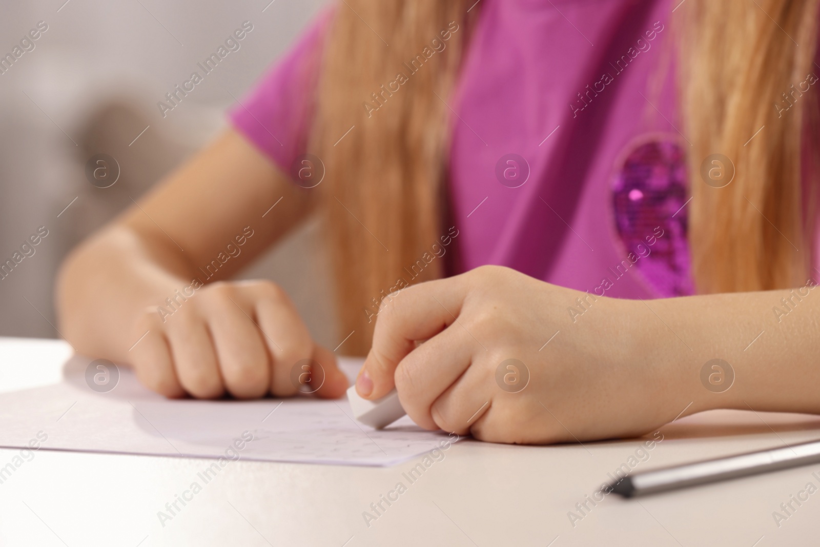 Photo of Girl erasing mistake in her homework at white desk indoors, closeup