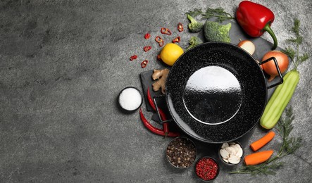 Photo of Empty iron wok surrounded by ingredients on grey table, flat lay. Space for text