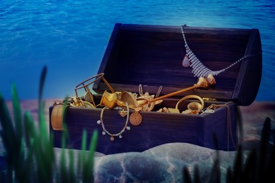 Open wooden chest full of treasures on sand seabed