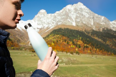 Photo of Boy drinking from thermo bottle in mountains on sunny day. Space for text