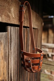 Brown dog muzzle hanging near wooden fence