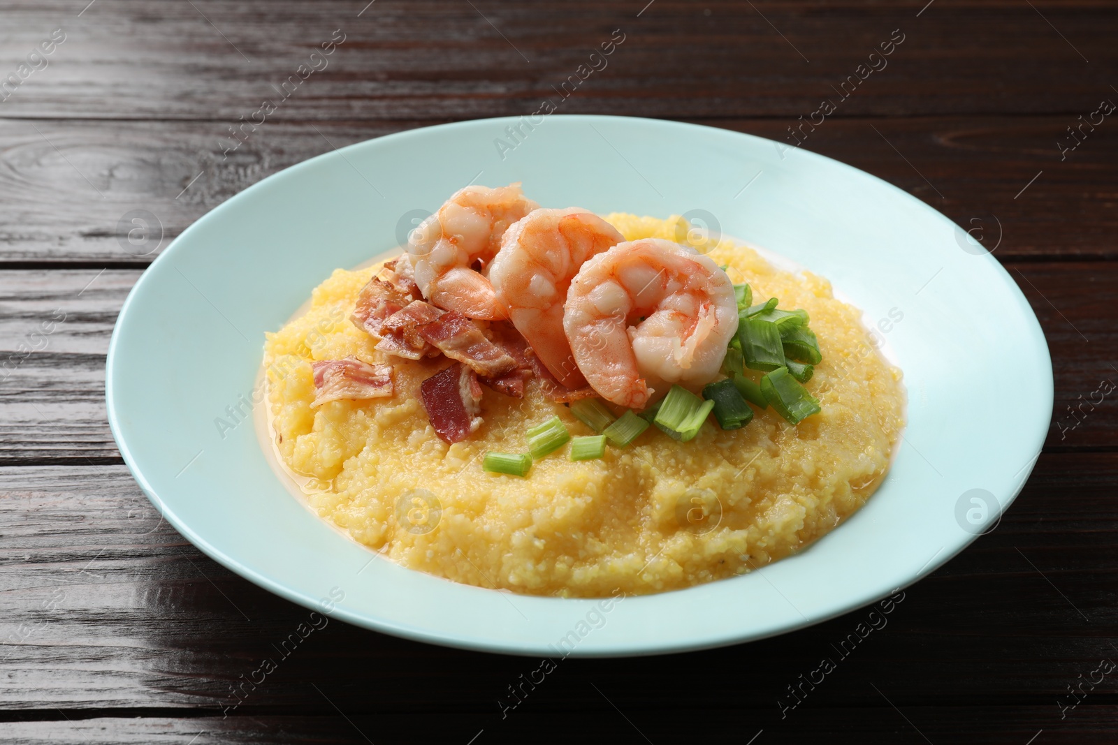 Photo of Plate with fresh tasty shrimps, bacon and grits on dark wooden table