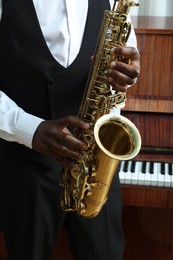 Photo of African-American man playing saxophone indoors, closeup. Talented musician