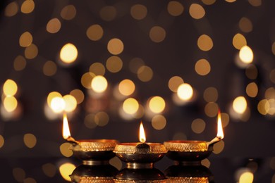 Photo of Lit diyas on table against blurred lights. Diwali lamps