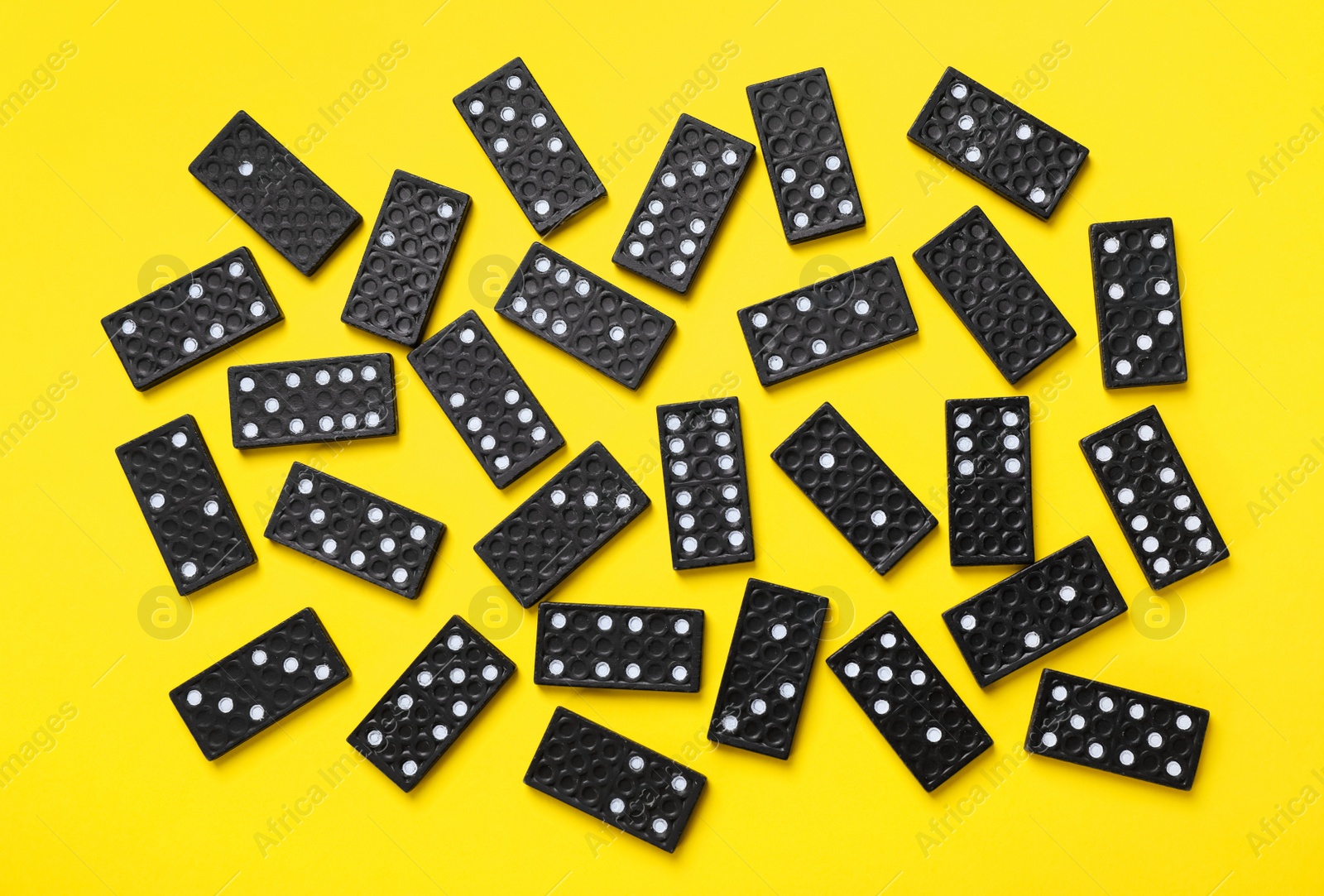 Photo of Black domino tiles on yellow background, flat lay