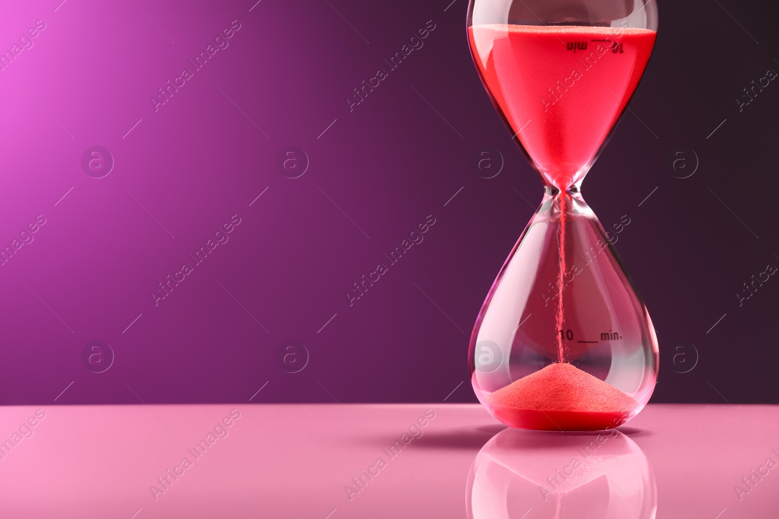 Photo of Hourglass with red flowing sand on color background, space for text