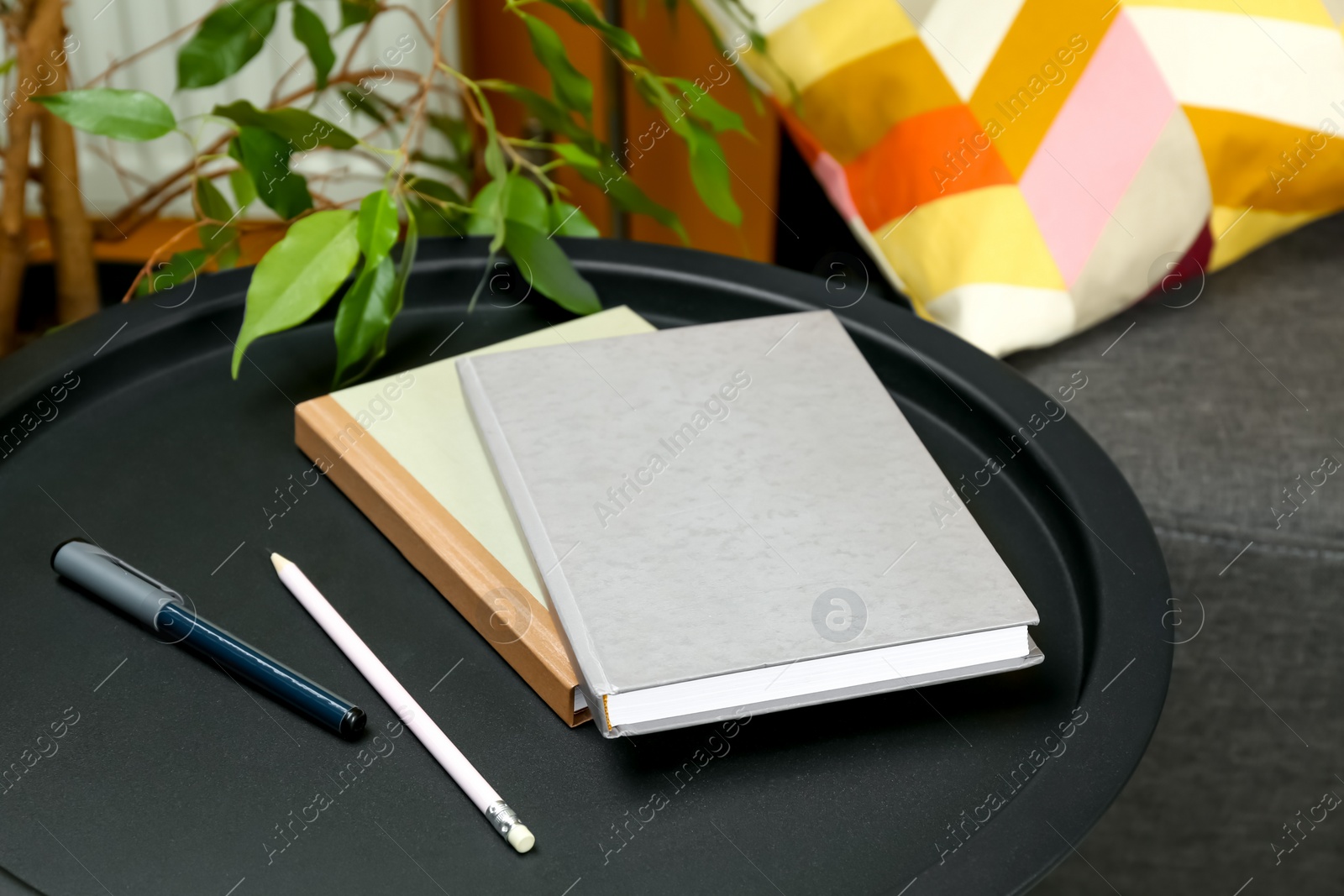 Photo of Books, pen and pencil on black table near sofa indoors, closeup