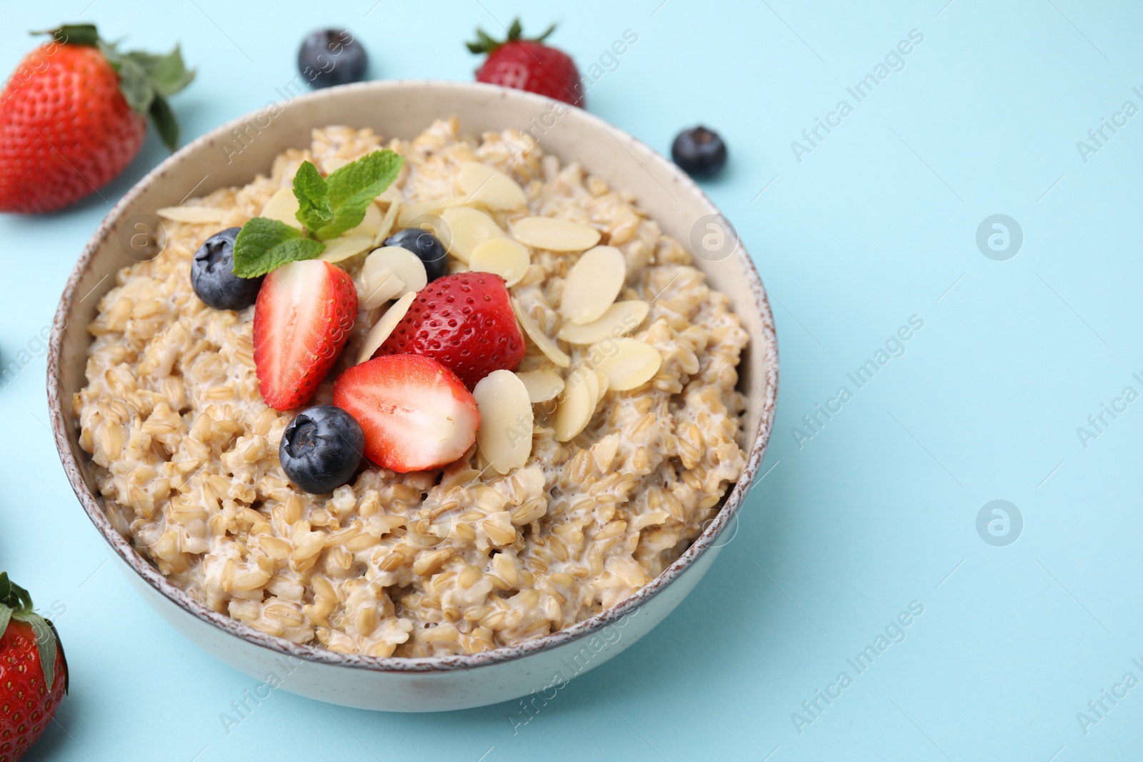 Photo of Tasty oatmeal with strawberries, blueberries and almond flakes in bowl on light blue background. Space for text