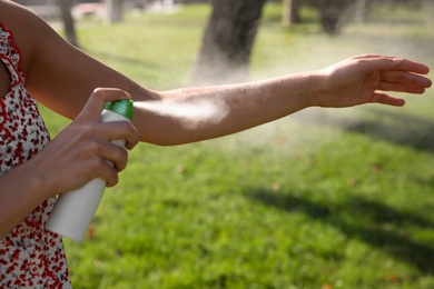 Woman applying insect repellent onto hand in park, closeup