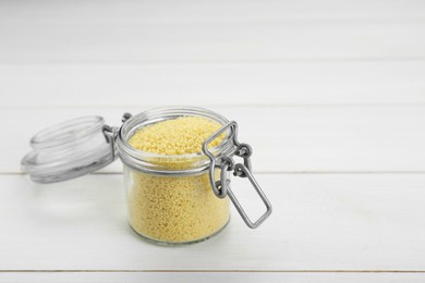 Glass jar of raw couscous on white wooden table. Space for text