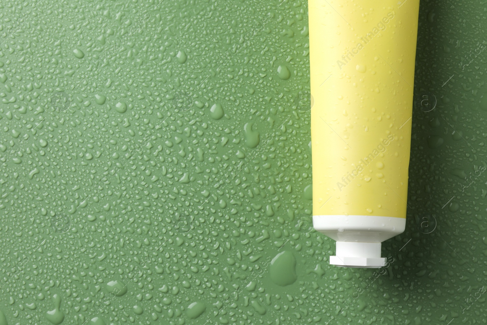 Photo of Moisturizing cream in tube on green background with water drops, top view. Space for text