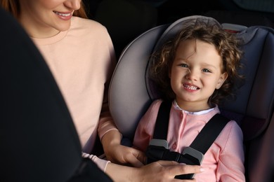 Photo of Mother fastening her daughter in child safety seat inside car