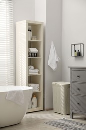 Stylish bathroom interior with grey chest of drawers and shelving unit