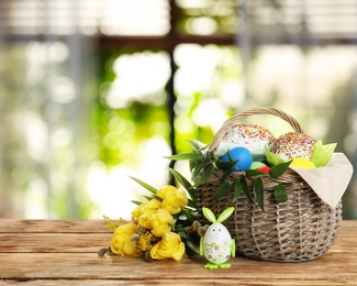 Image of Basket with delicious Easter cakes, dyed eggs and flowers on wooden table indoors. Space for text