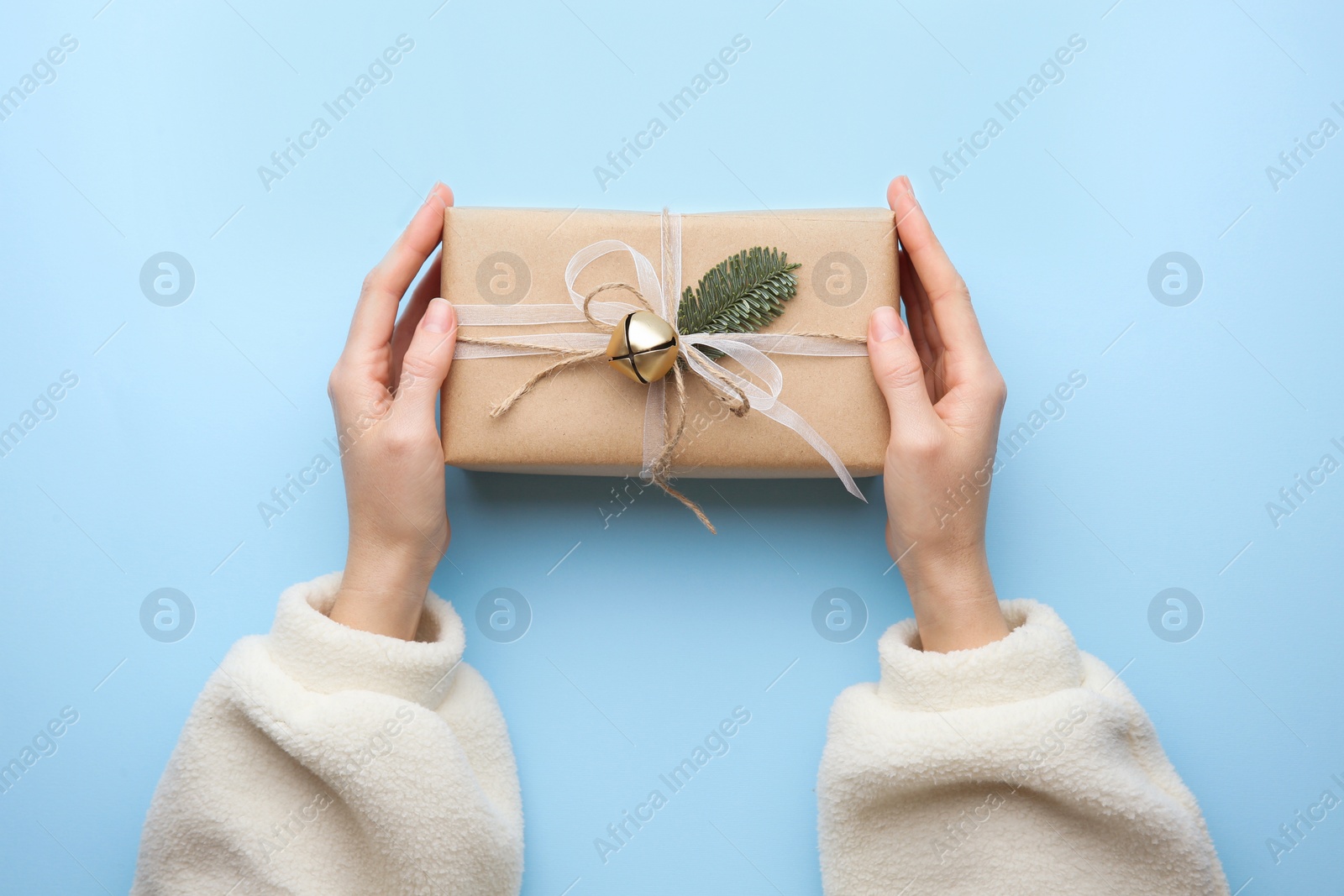 Photo of Woman holding Christmas gift box on light blue background, top view