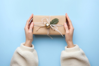 Photo of Woman holding Christmas gift box on light blue background, top view