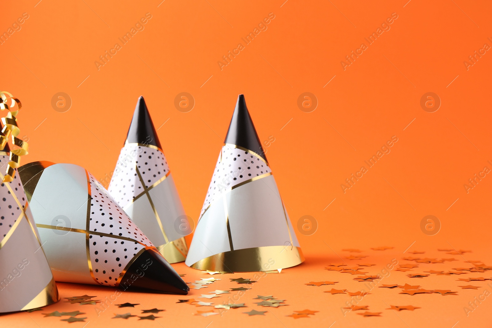Photo of Party hats and confetti on orange background, space for text