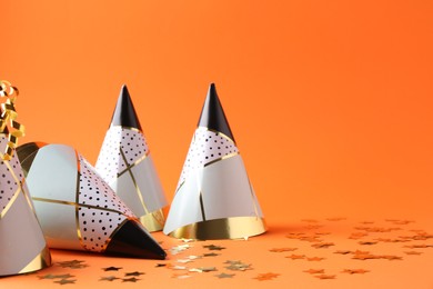 Party hats and confetti on orange background, space for text