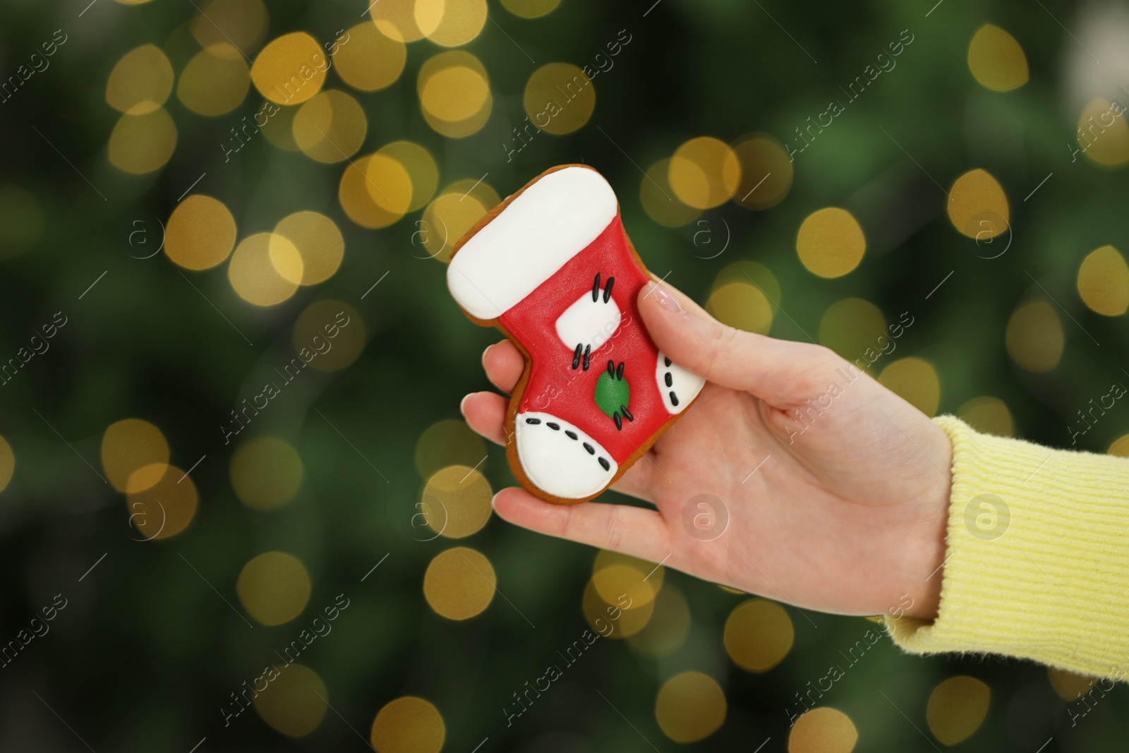 Photo of Woman with decorated cookie against blurred Christmas lights, closeup