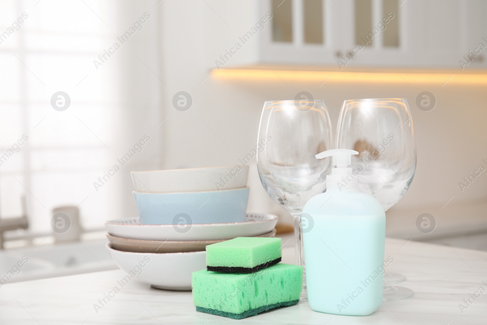 Photo of Set of clean dishes and cleaning product with sponge on table in stylish kitchen