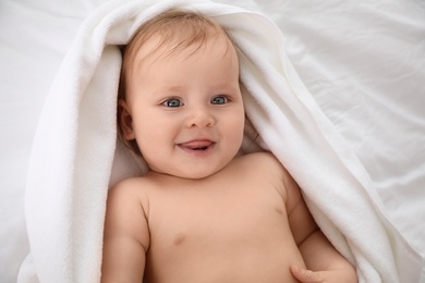 Photo of Cute little baby with soft towel lying on bed after bath