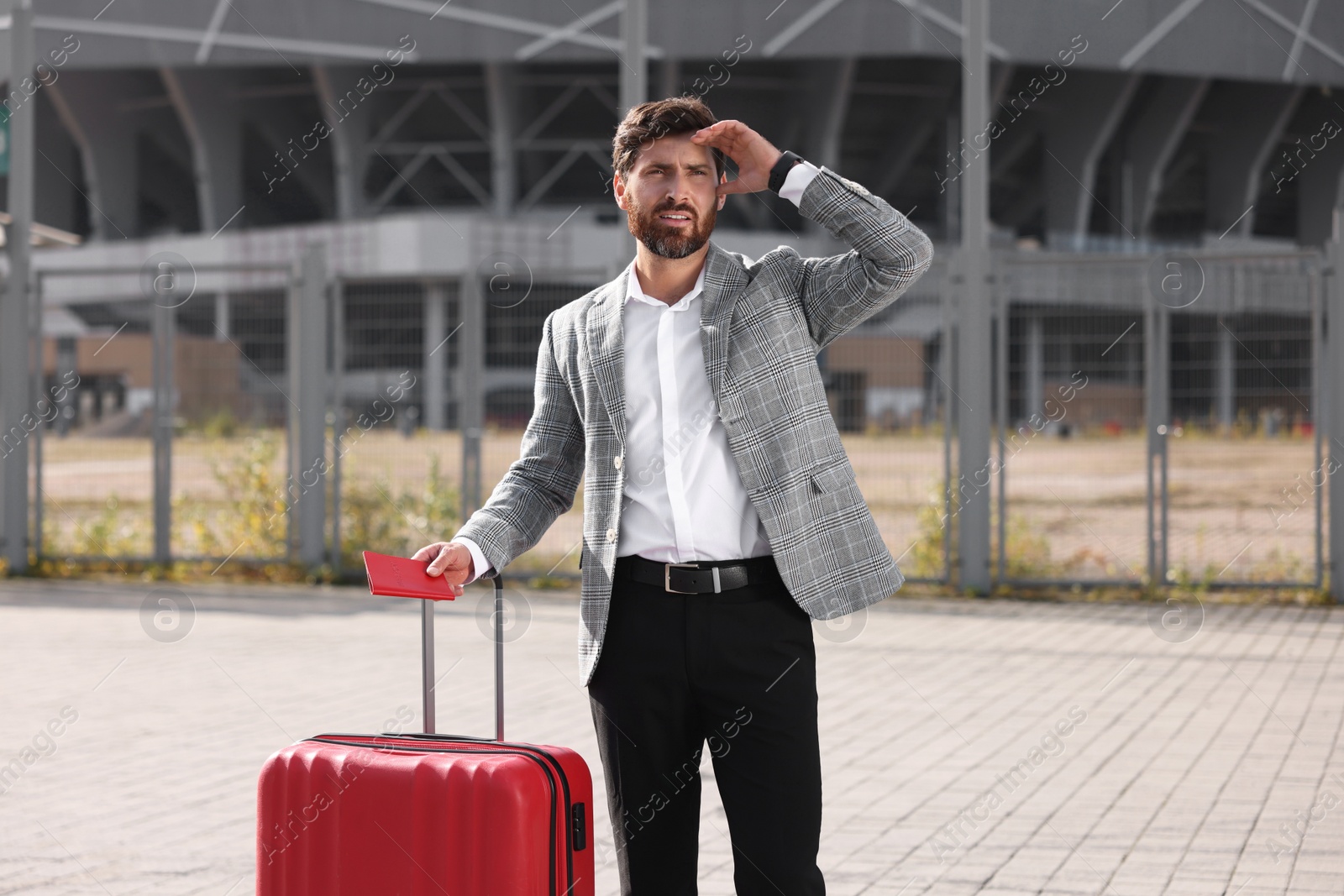 Photo of Being late. Worried businessman with red suitcase and passport outdoors