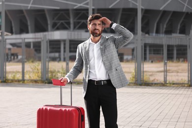 Being late. Worried businessman with red suitcase and passport outdoors