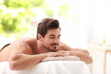 Handsome young man relaxing on massage table in spa salon, space for text