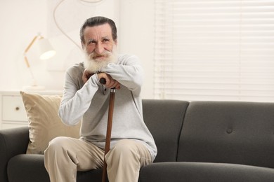 Senior man with walking cane on sofa at home