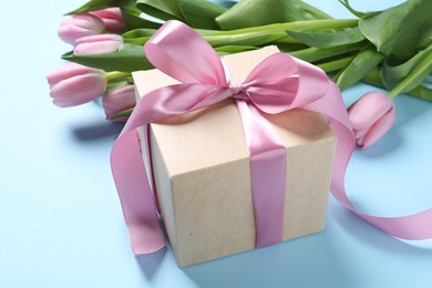 Photo of Beautiful gift box with bow and pink tulip flowers on light blue background, closeup
