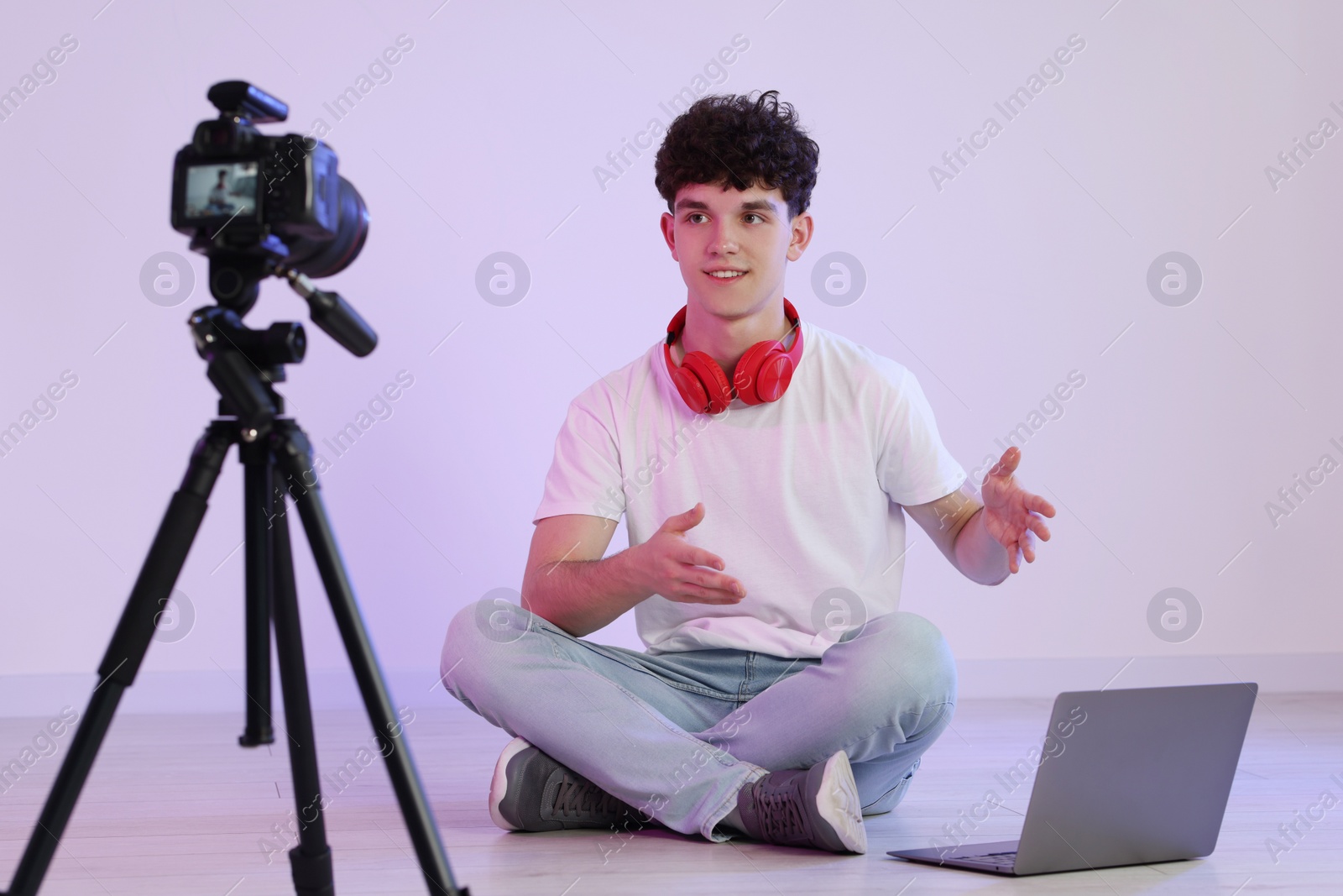 Photo of Smiling teenage blogger with laptop explaining something while streaming indoors