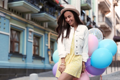 Photo of Beautiful young woman with color balloons on city street