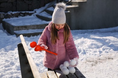 Photo of Cute little girl playing with snowball maker outdoors