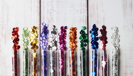 Photo of Tubes with many colorful sequins on white wooden table, flat lay