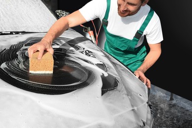 Worker washing auto with sponge at outdoor car wash, closeup
