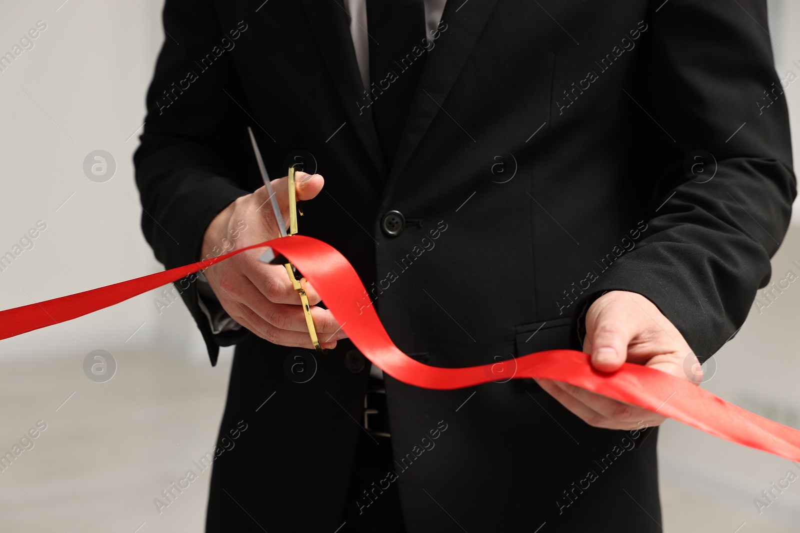 Photo of Man cutting red ribbon with scissors on blurred background, closeup