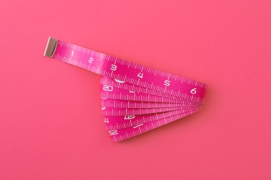 Measuring tape on pink background, top view